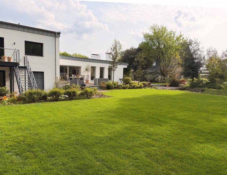 Professionell gepflegter Garten mit sattgrüner Rasenfläche und gestalteter Außenanlage bei modernem Wohnhaus