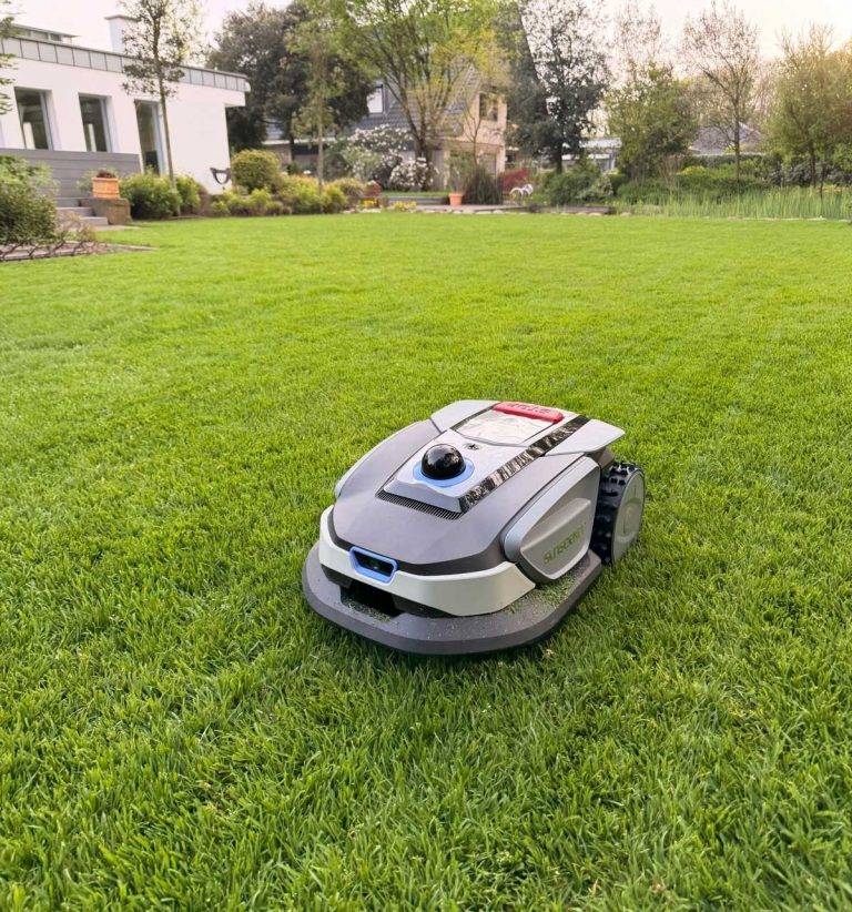 Moderner Mähroboter fährt autonom über einen gleichmäßig gemähten Rasen vor einem Einfamilienhaus – automatisierte Rasenpflege von Gartenkonzepte
