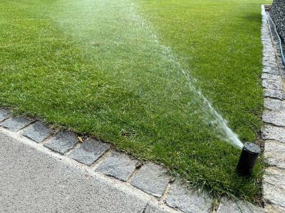Eingebauter Sprinkler bewässert automatisch eine gepflegte Rasenfläche mit Pflasterstein-Einfassung – Bewässerungssystem von Gartenkonzepte