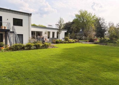 Professionell gepflegter Garten mit sattgrüner Rasenfläche und gestalteter Außenanlage bei modernem Wohnhaus