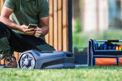 Techniker konfiguriert einen Mähroboter auf dem Rasen – fachgerechte Installation, Programmierung und Wartung von Mährobotern durch Gartenkonzepte Dresden