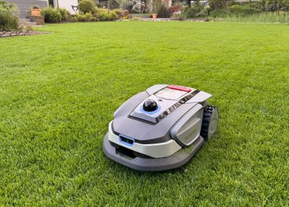 Moderner Mähroboter fährt autonom über einen gleichmäßig gemähten Rasen vor einem Einfamilienhaus – automatisierte Rasenpflege von Gartenkonzepte
