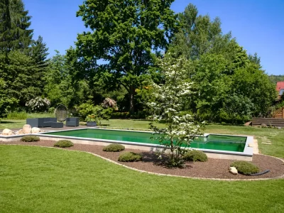 Weitläufiger Privatgarten mit Naturpool, Rindenmulch-Rundbeet, Zierbaum und Outdoor-Lounge bei strahlendem Sonnenschein