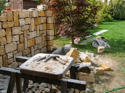 Handwerklicher Bau einer Natursteinmauer mit Werkzeug und Steinmaterial im Garten – Gartengestaltung Dresden