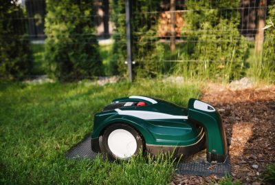 Grüner Mähroboter dockt an seiner Ladestation im naturnahen Garten an – automatisierte Rasenmähtechnik von Gartenkonzepte