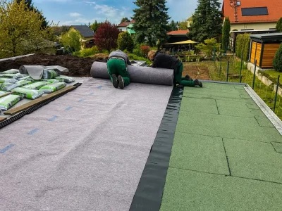 Zwei Mitarbeiter in grüner Arbeitskleidung verlegen Rollrasen in einem neuen Garten – professionelle Rasenpflege
