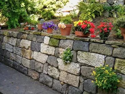 Rustikale Trockenmauer aus Naturstein mit farbenfrohen Blumentöpfen und Bepflanzung in der Gartengestaltung